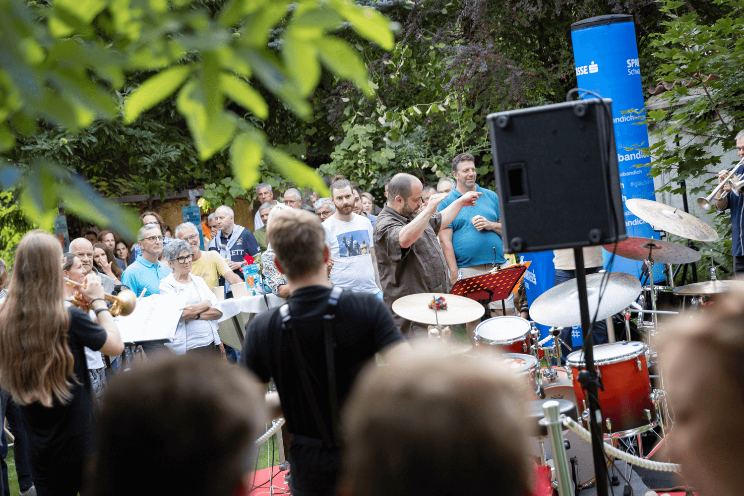 Outreach-Ensemble mit Dirigent und Publikum in Hintergrund.