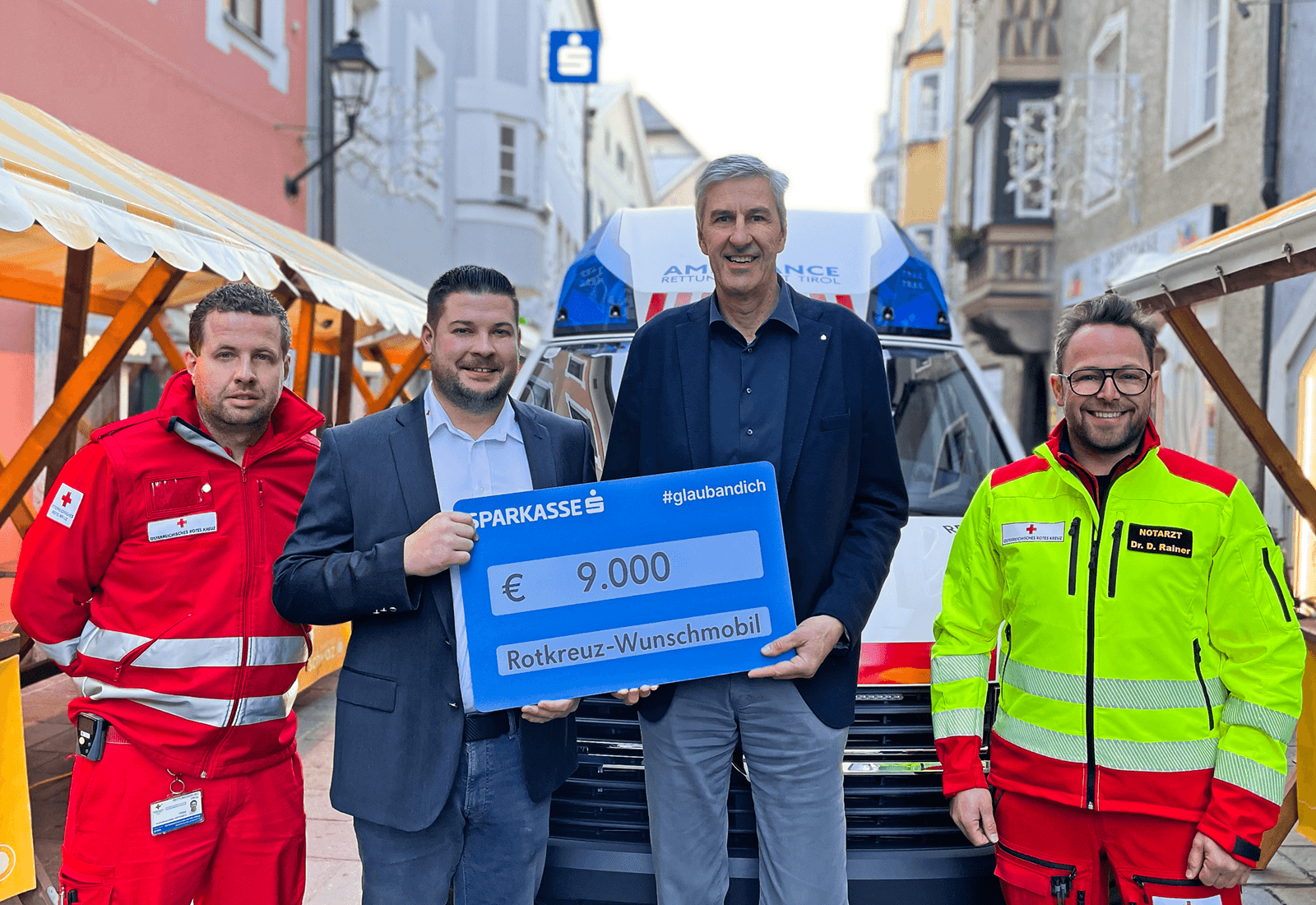 Fuhrparkverantwortlicher Martin Sporer, Dominik Hasenberger (beide Rotes Kreuz), VDir. Johannes Haid und Daniel Rainer (Bezirksstellenleiter Stv., Rotes Kreuz) bei der Scheckübergabe in der Schwazer Innenstadt vor einem Rettungswagen.
