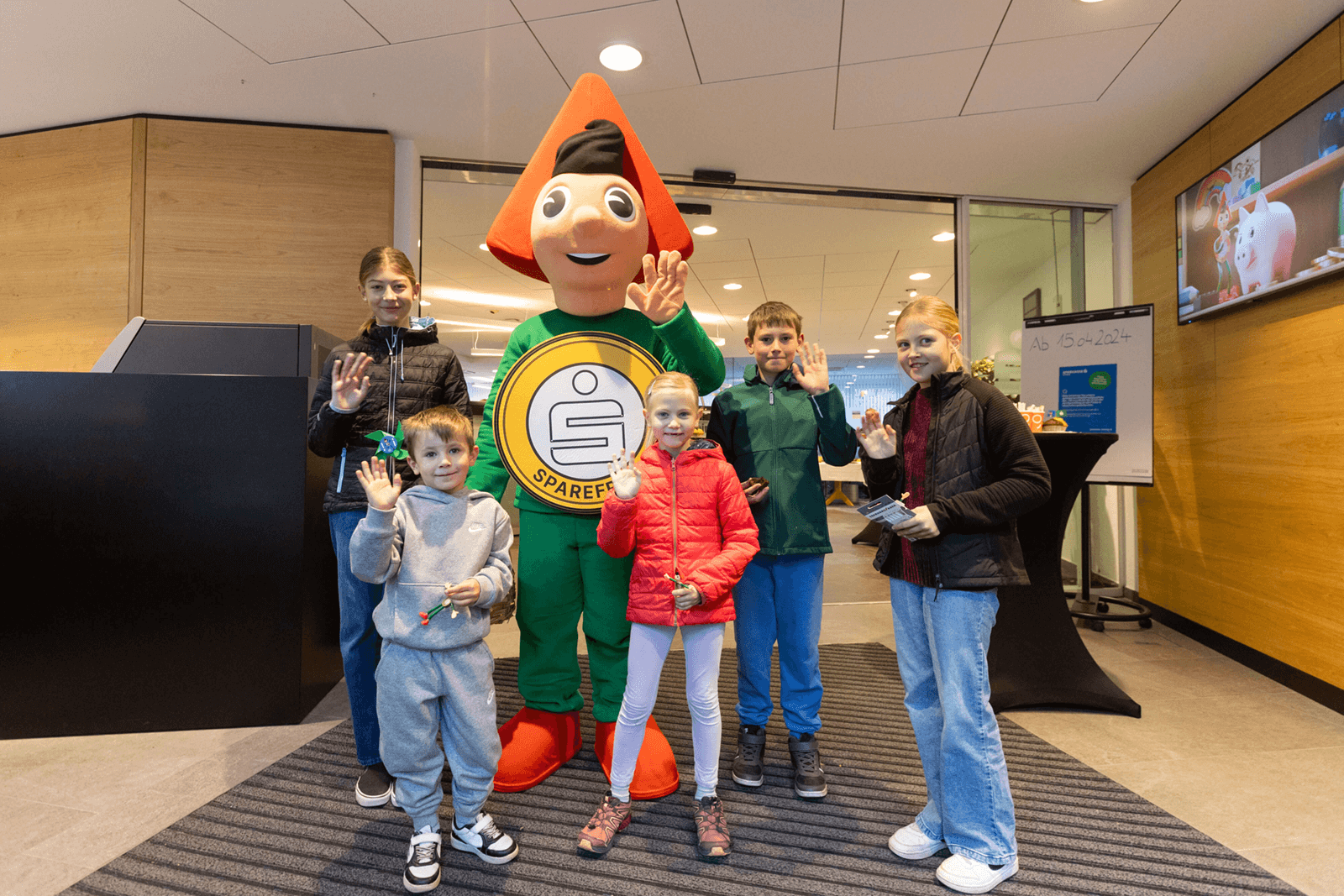 Winkende Kinder mit dem Sparkassen-Maskottchen Sparefroh.