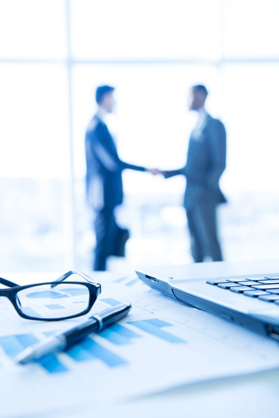 Business Focus on the things on the table. Blurred men near panoramic windows on background.