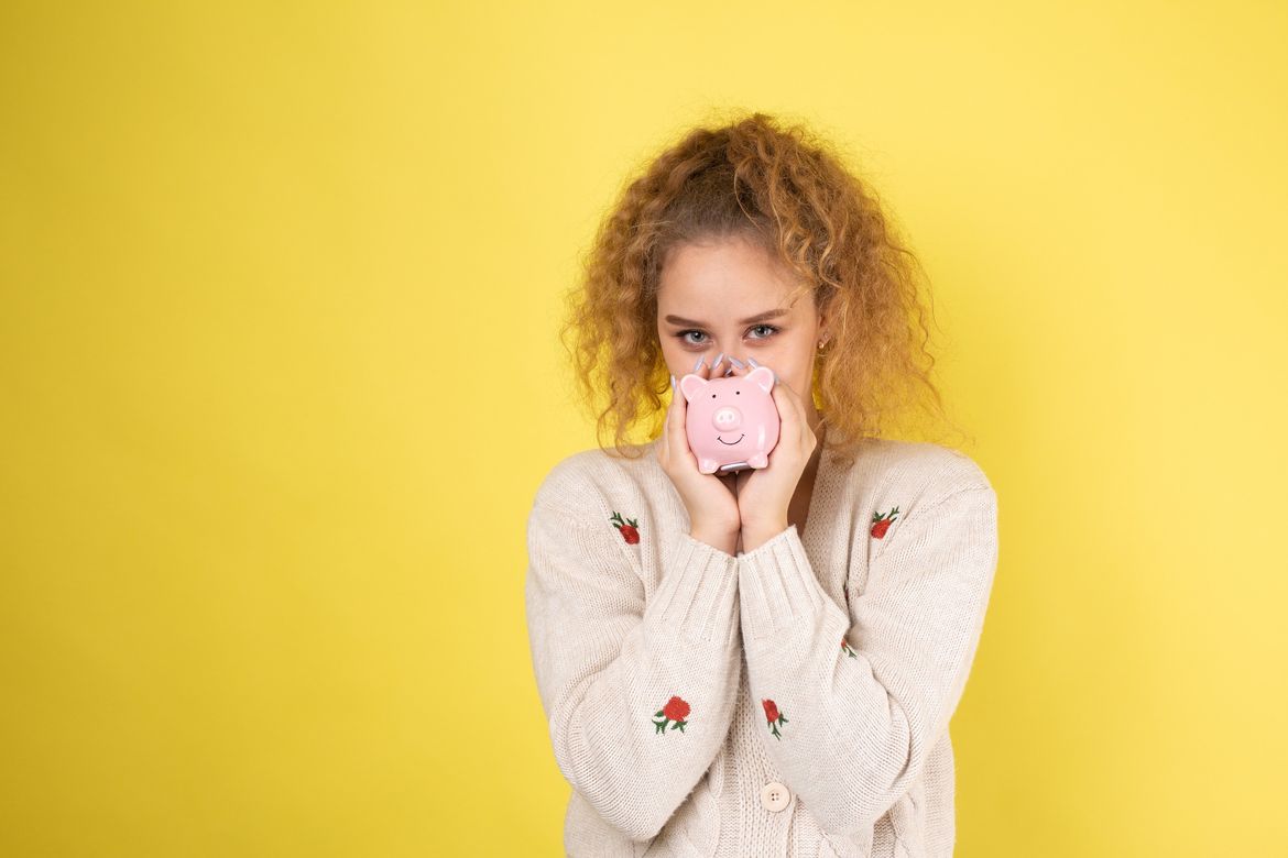 A cute young girl with curly red hair holds a piggy bank, a pink piglet in her hands. The concept of wealth and safety of money.