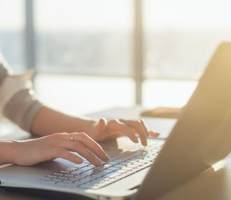 Female writer typing using laptop keyboard at her workplace in the morning. Woman writing blogs online, side view close-up picture.