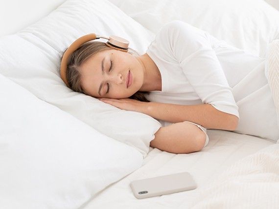 žena ležící na posteli s bezdrátovými sluchátky na hlavě