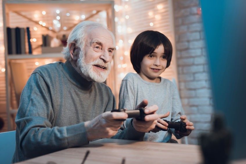 Grandfather and grandson are playing video games on computer at night at home.