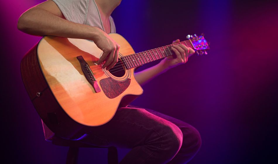 The musician plays an acoustic guitar. Beautiful background with colored light rays.