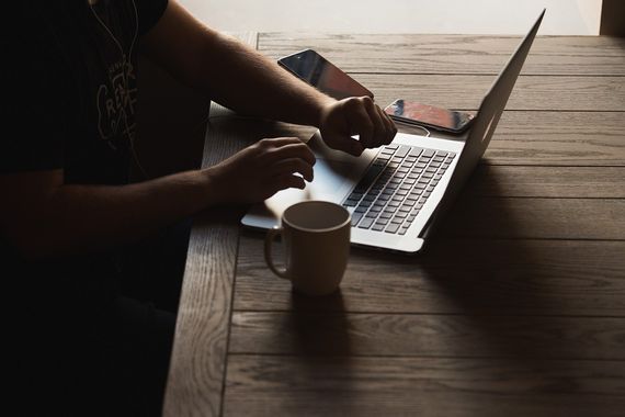 Člověk pracující na notebooku u dřevěného stolu s kávou