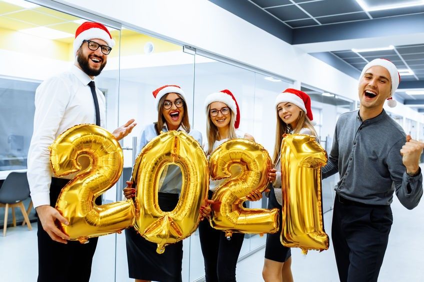 Office Christmas party. group of joyful colleagues in Santa Claus hats, having fun and celebrating the New Year, holding balloons with a golden number, a symbol of 2021