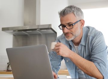 Mann mit Laptop am Küchentisch sitzend.