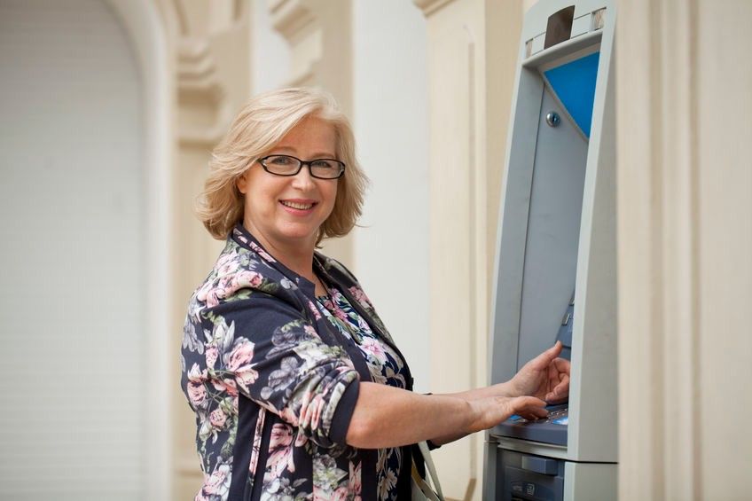 Mature blonde woman counting money near ATM