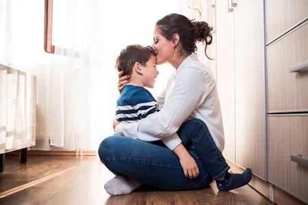 Beautiful young mom and her son. Mom is kissing her kid in the forehead.