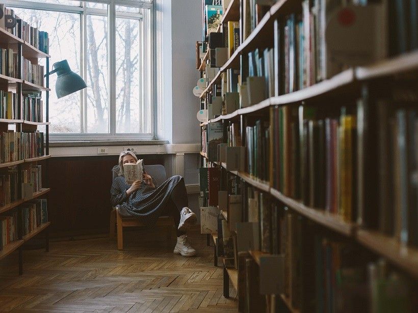 Žena si čte v křesle v knihovně