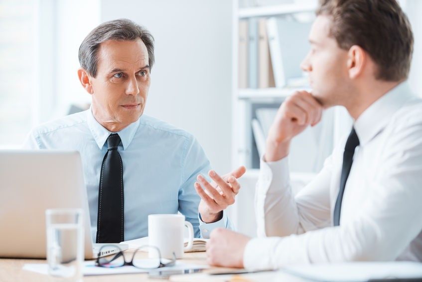 Wise advice for business nice. Two business people in formalwear discussing something while sitting at working place
