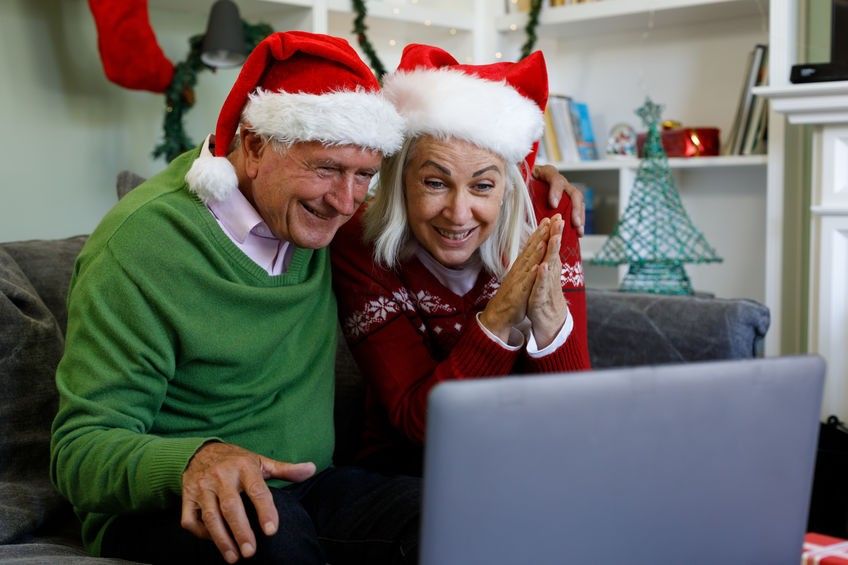 Senior couple in santa hat sitting on couch smiling while having a video call on laptop at home
