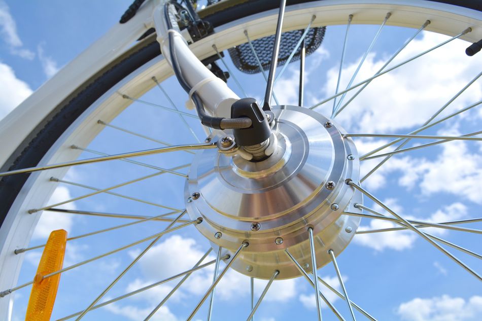Wheel of the electric bicycle view from below. E bike motor with light reflections. Unfiltered, with natural lighting and blue sky and clouds.