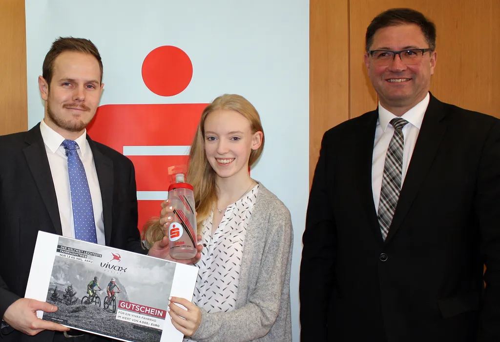 Mädchen hält Stift und Gutschein in der Hand und nebenan stehen zwei Männer 