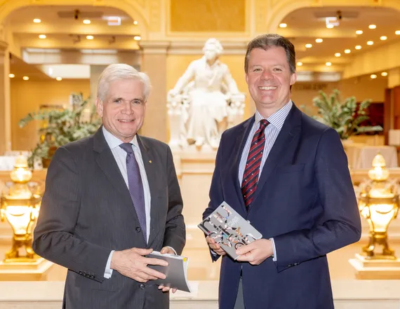 2 Männer in Anzügen, die jeweils ein Programmheft des Musikvereins in Händen halten