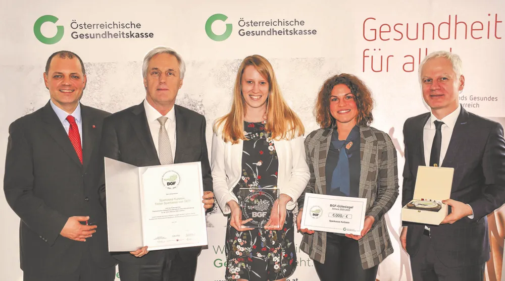 5 Personen stehen vor einem ÖGK Aufsteller und lächeln in die Kamera, in den Händen haben sie einen Preis sowie eine Urkunde