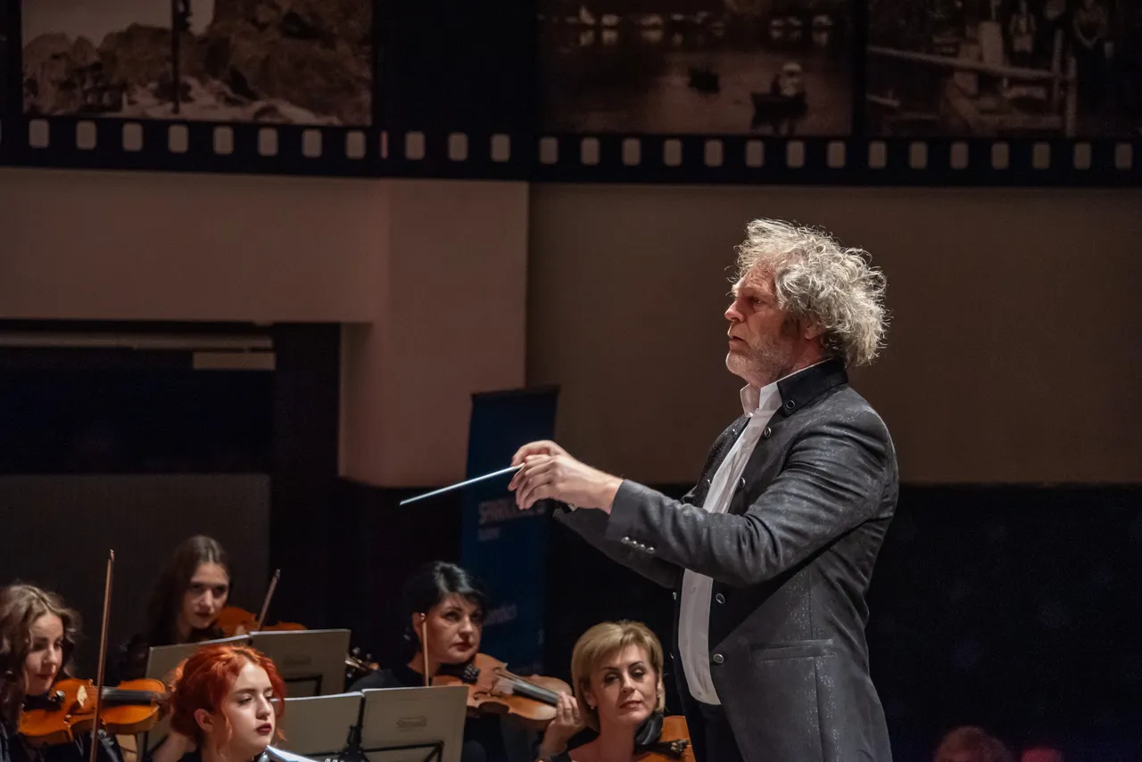Dirigent mit Taktstock, im Hintergrund das Orchester