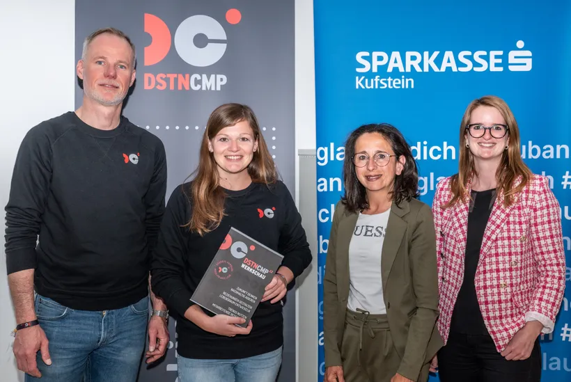 4 Personen stehen vor einem DSTNCMP und einem Sparkasse Kufstein Aufsteller und lachen in die Kamera