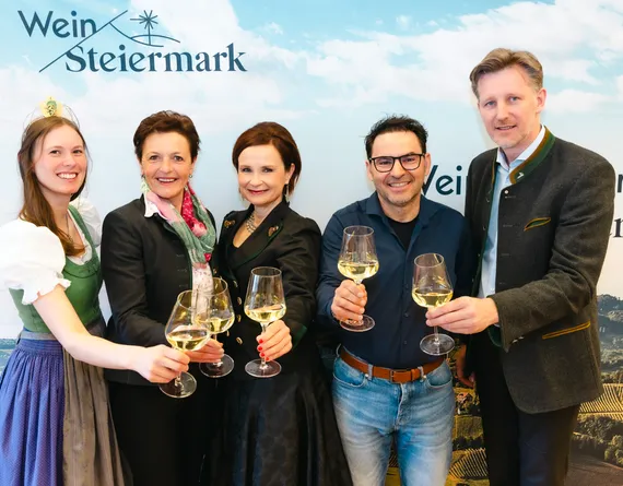 Fünf Personen, drei Frauen und zwei Männer stehen nebeneinander und halten jeweils ein Weinglas in die Kamera.er Frau, alle lächeln.