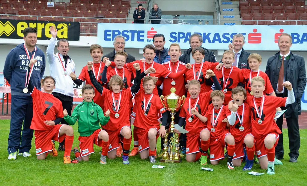 Gruppenbild von Jugendlichen Fußballern auf Spielfeld mit Medaille und Pokal in der Hand