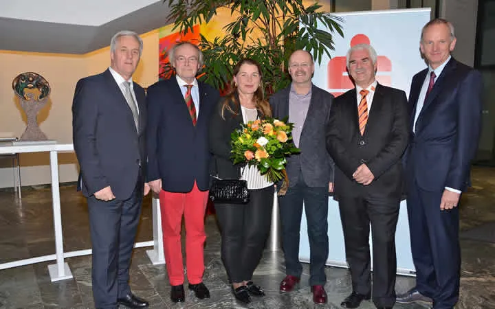 eine stehende Frau mit Blumen in der Hand und fünf Männer stehen nebenan