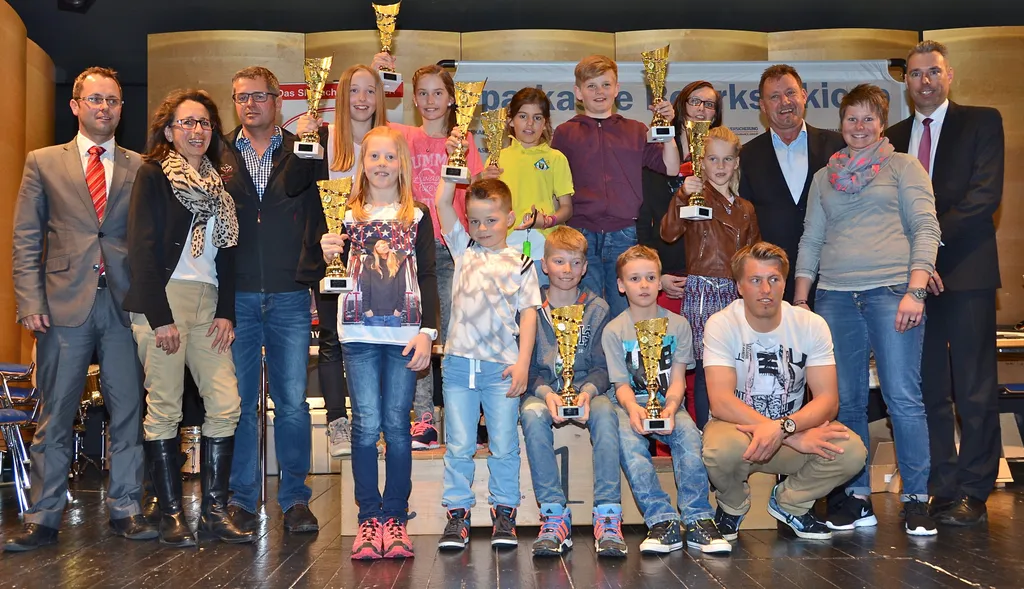 Kinder mit Pokal in der Hand und Männer und Frauen nebenan
