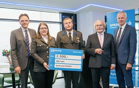 5 Personen stehen nebeneinander für das Foto, zwei halten einen Scheck in der Hand