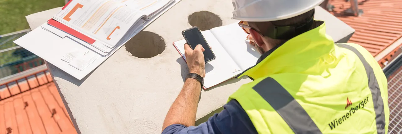 Arbeiter mit Plan, Handy und Wienerberger-gebrandeter Jacke