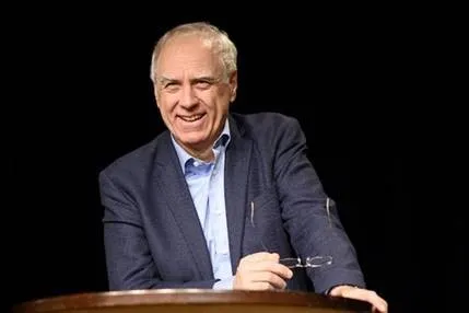 Herr an Rednerpult mit Brille in der Hand lächelt ins Publikum