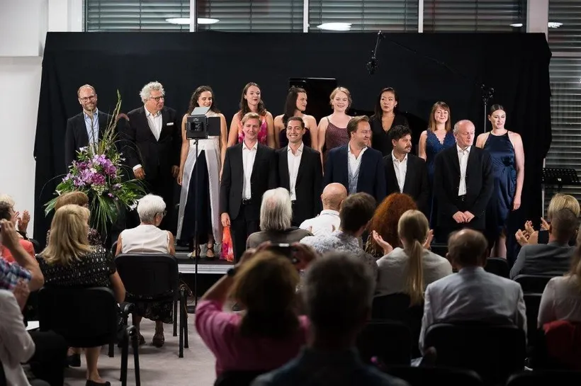 Künstler stehen lächelnd auf der Bühne, Publikum von hinten