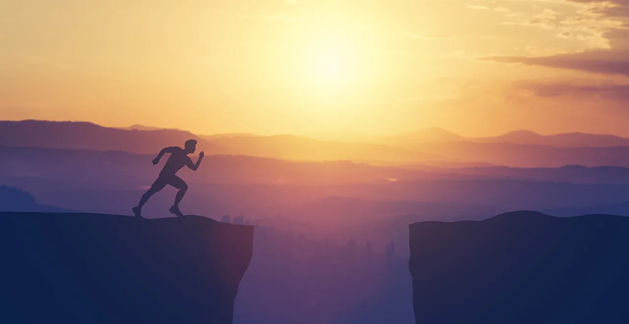 Mann nimmt Anlauf um über eine Felsenspalte zu springen