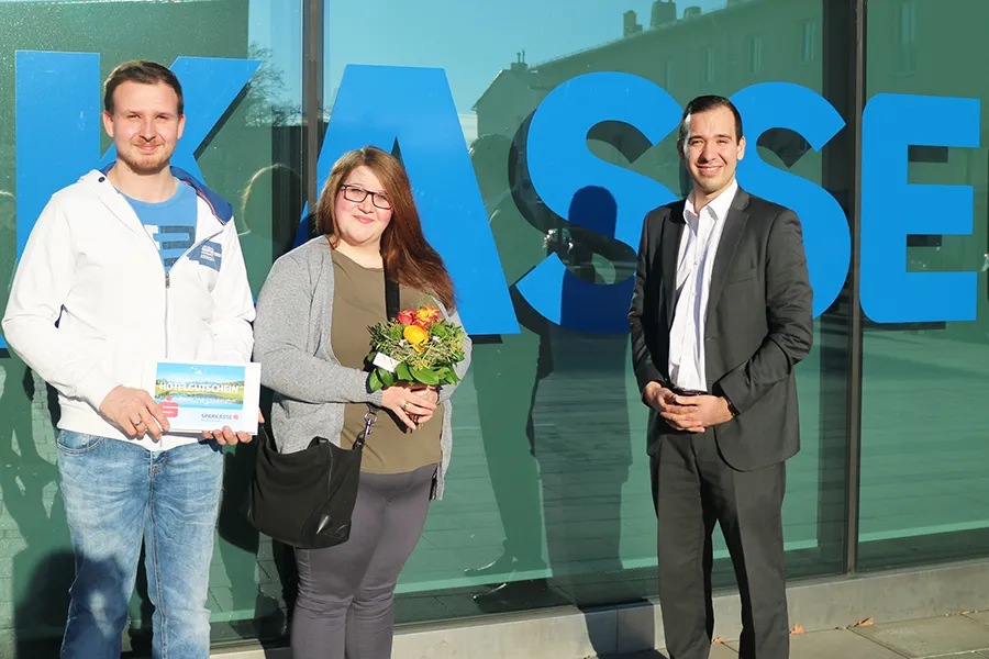 Kundenbetreuer Sebastian Ebner (rechts) übergibt den glücklichen Gewinnern Melanie und Matthias Hardteck ihren Hochzeitsreise-Gutschein in der Sparkassen-Filiale Ternitz.