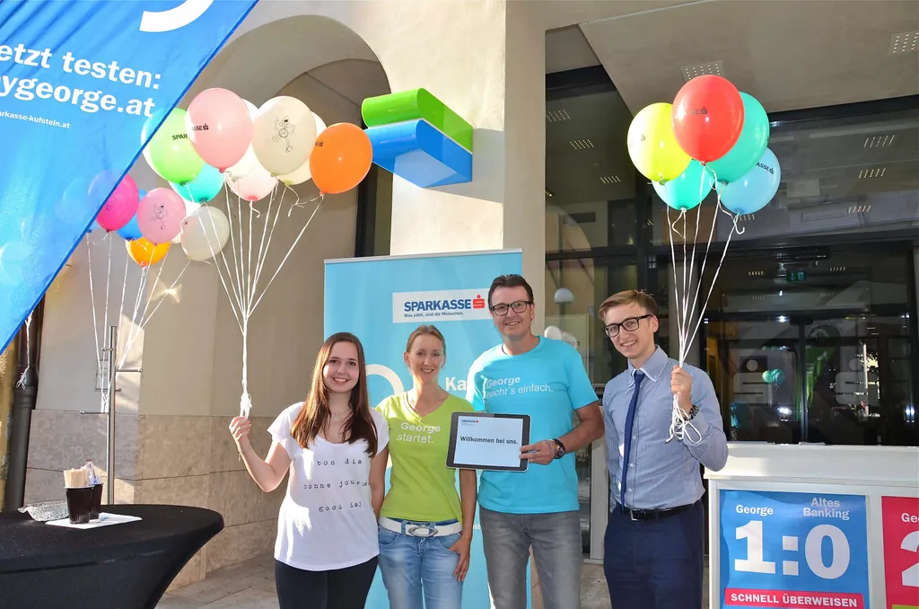 zwei Frauen und zwei Männer vor Sparkasse Eingang mit Luftballon in der Hand 