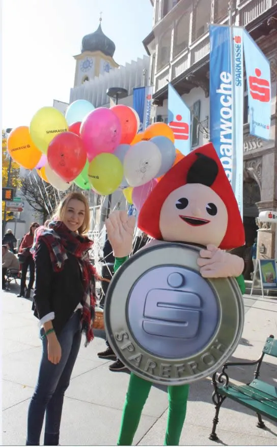 eine stehende Frau neben dem Sparkasse Maskottchen 