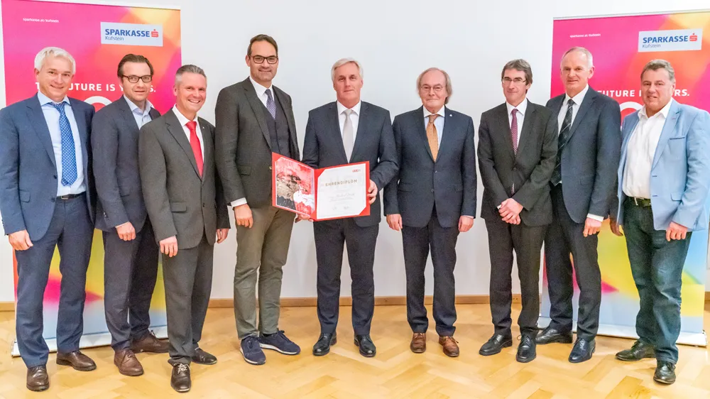 Eine Gruppe von Herren im Anzug stehen nebeneinander vor einem Sparkasse Aufsteller und lächeln
