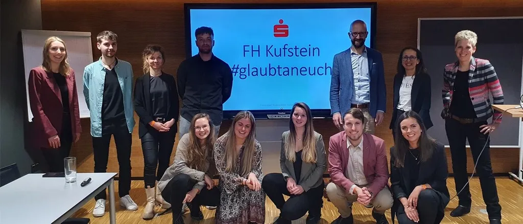 Gruppenfoto in Konferenzraum, Leinwand mit dem Text FH Kufstein #glaubtaneuch 