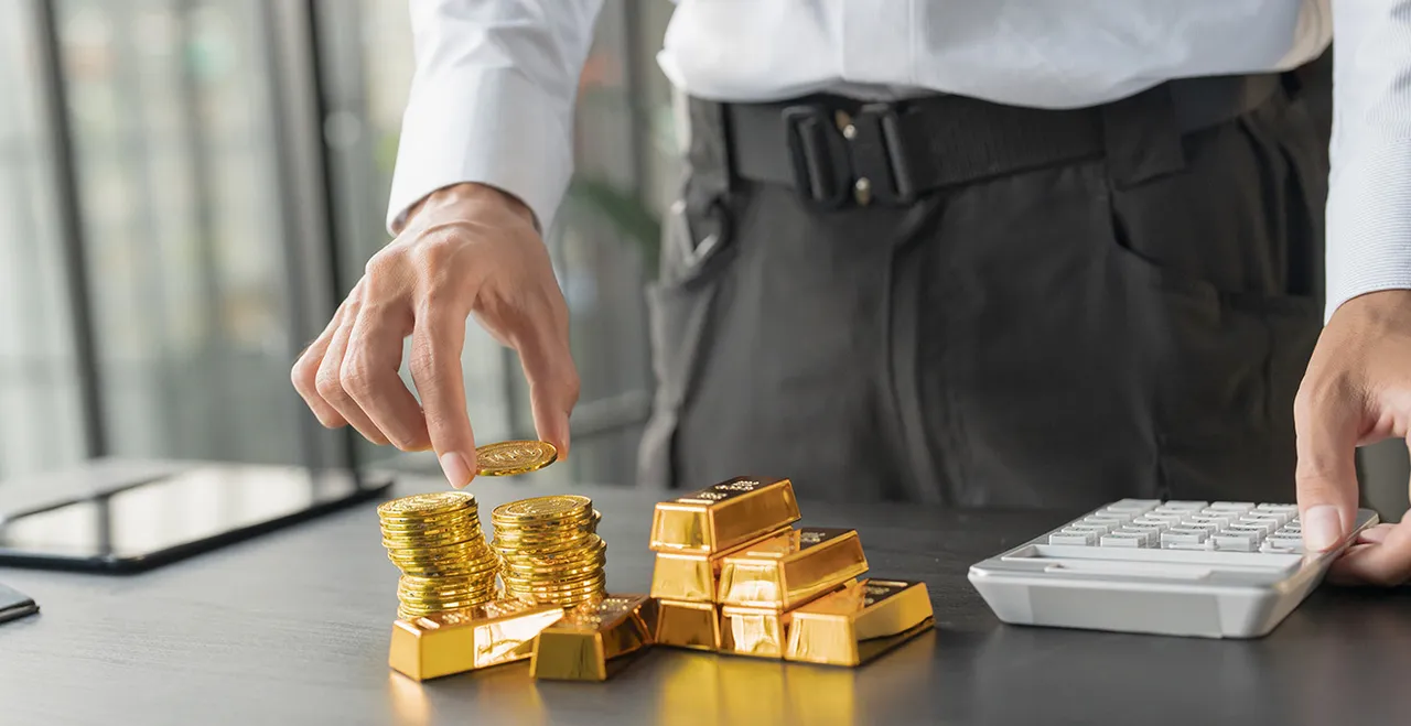 Businessmann mit Rechner, Goldmünzen und Goldbarren