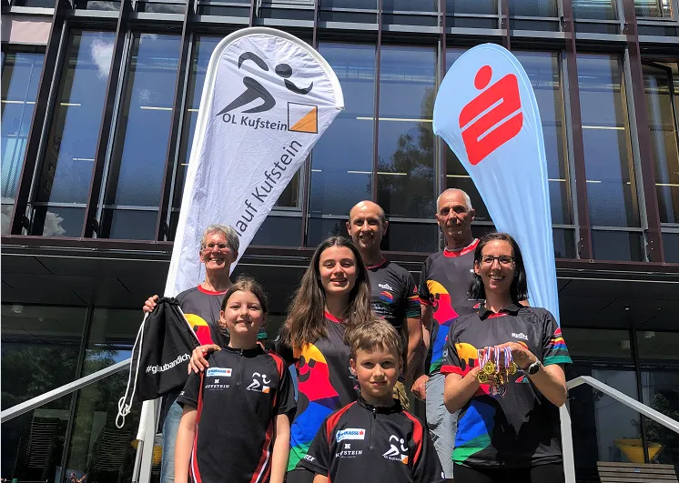 Kinder und Erwachsene mit sportlichem Shirt lächeln bei Sonnenschein in die Kamera