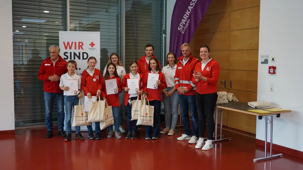 Kinder mit Rot-Kreuz-Jacke halten Urkunde und Sackerl und lächeln in die Kamera