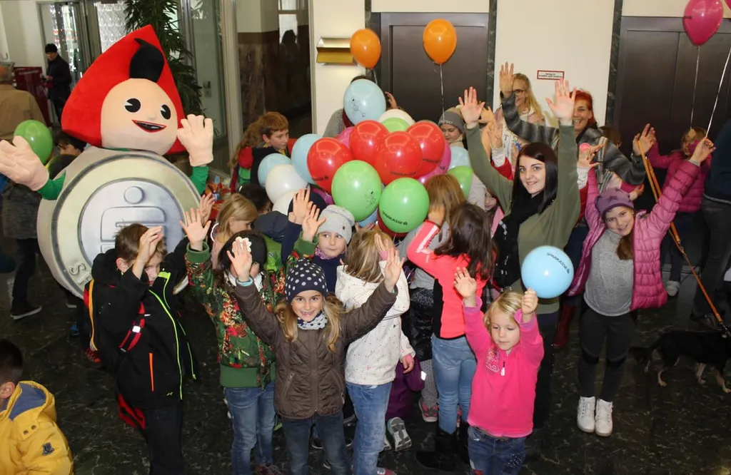 stehende Kinder mit Hände in der Höhe und Sparkasse Maskottchen 