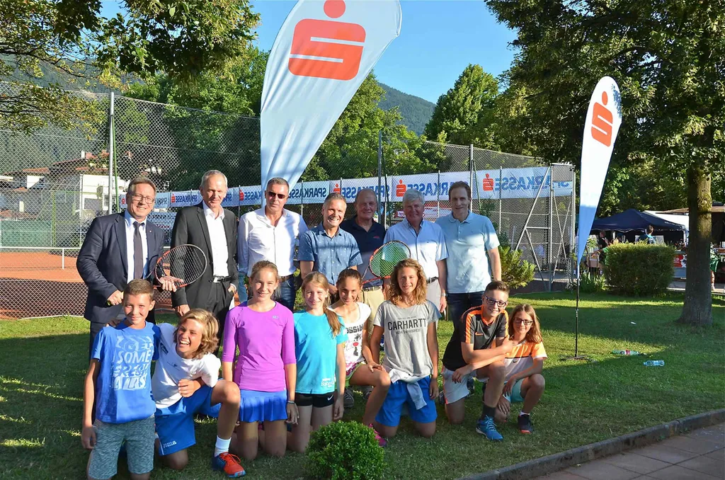 sieben Männer stehen hinter Kinder welche auf der Wiese knien 