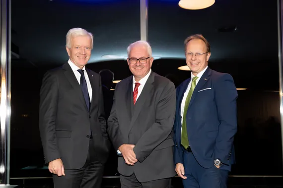 Drei Herren in dunklen Anzügen mit Krawatte