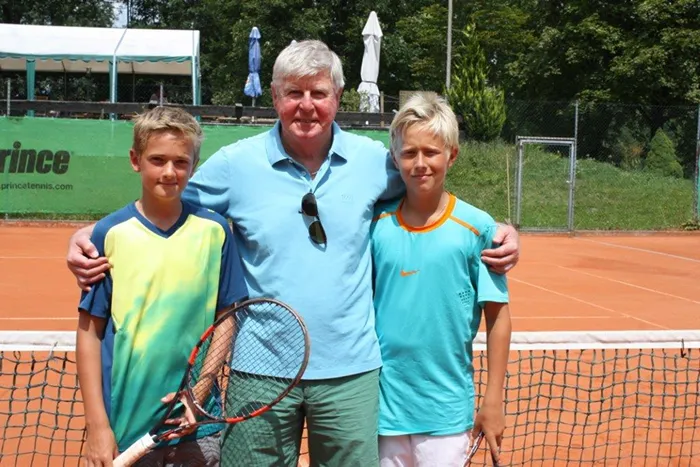 ein Mann und zwei Burschen mit Tennisschläger in der Hand schauen in die Kamera