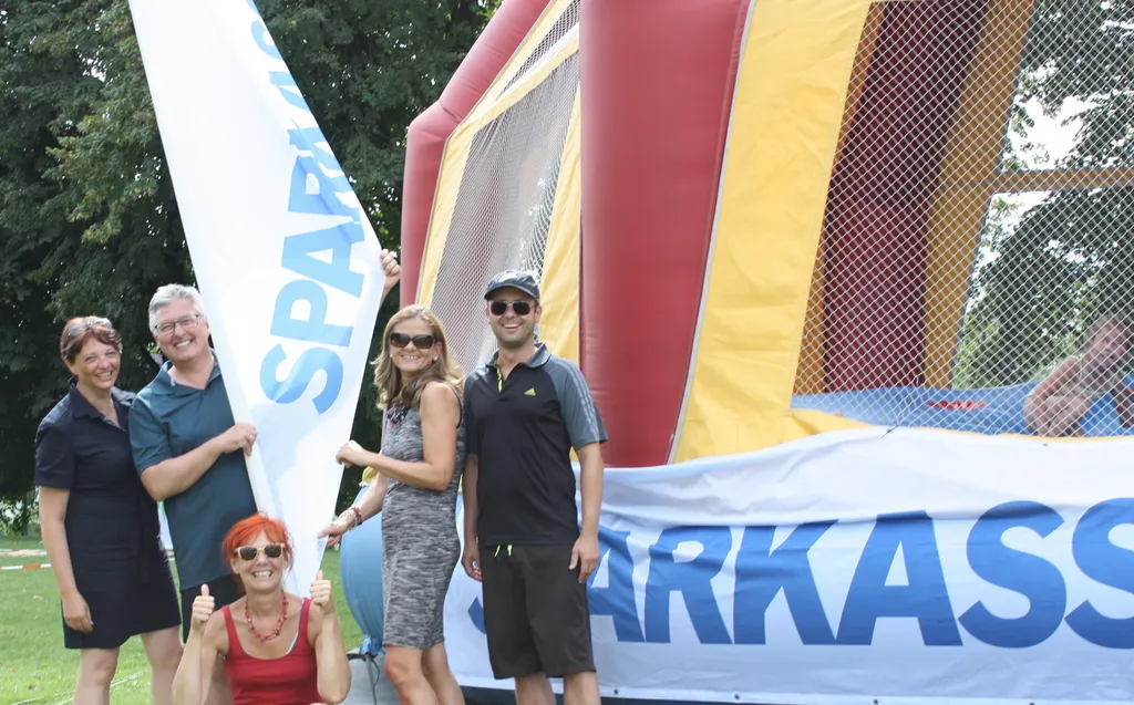 drei Frauen und zwei Männer stehen lachend neben Sparkasse Aufsteller