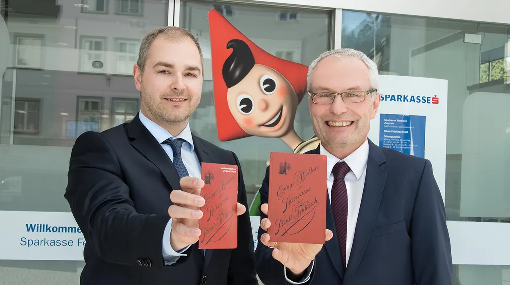 Foto (v.li.): Vorstandsdirektor Daniel Mierer mit dem neuen „Jubiläums-Sparbuch“ und Vorstandsdirektor Anton Steinberger mit dem über einhundert Jahre alten Vorbild …