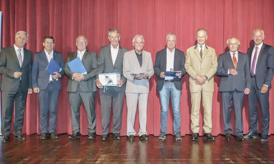 Gruppenfoto von Herren in Anzug vor einem roten Vorhang