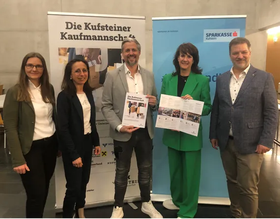 5 Personen stehen zusammen und zeigen eine Broschüre in die Kamera