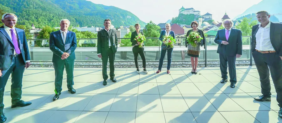 eine Gruppe von schön gekleideten Menschen steht im Halbkeis auf einem großen Balkon, die Damen haben einen Blumenstrauß