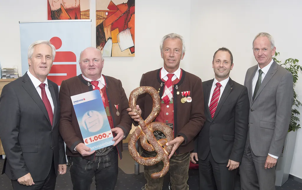 ein Mann hält eine große Brezel in der Hand und vier Männer stehen nebenan